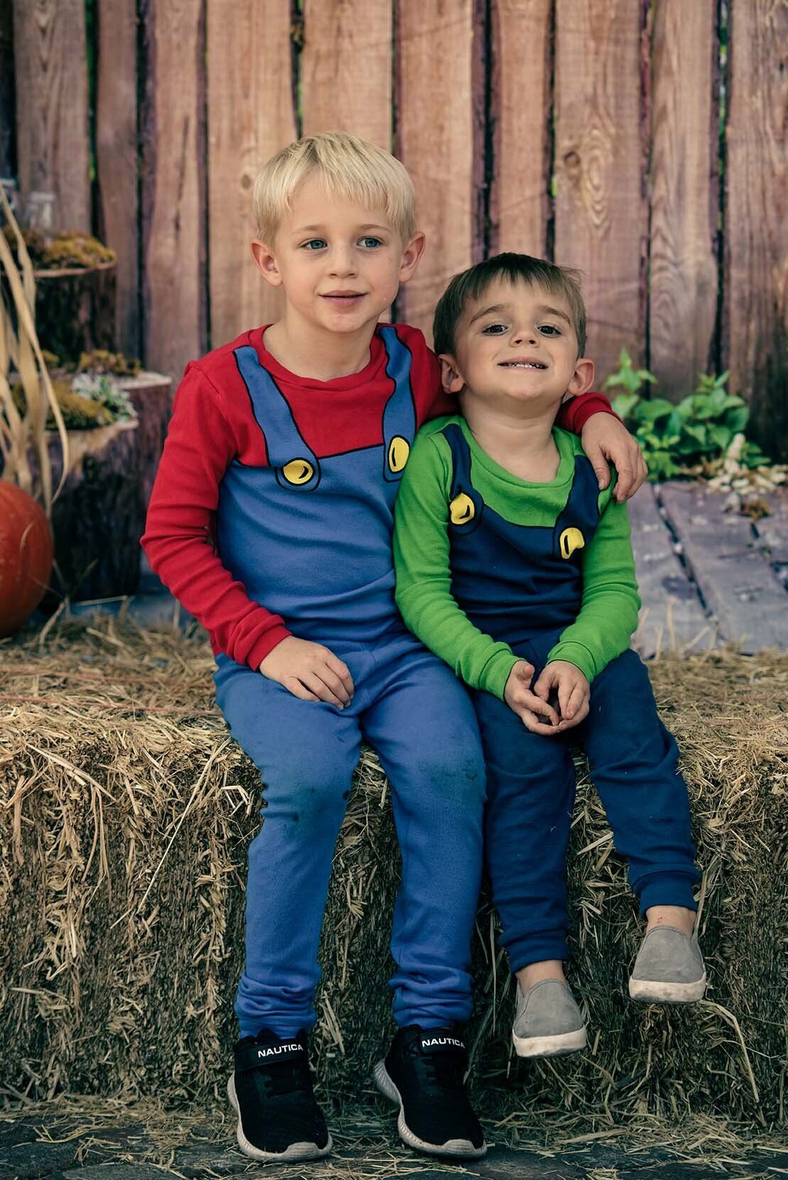Two young boys are sitting on a bale of hay.