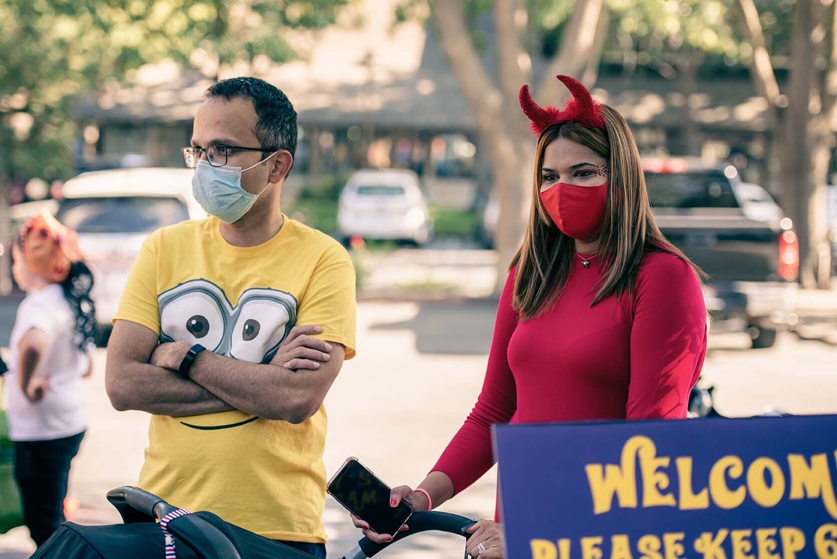 A man and a woman wearing masks are standing next to a sign that says welcome.