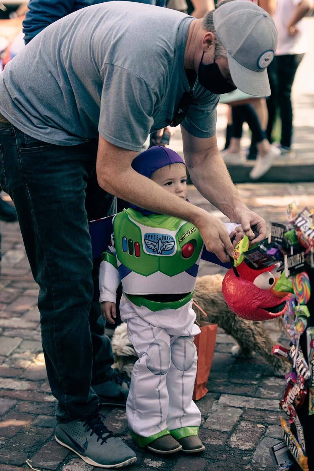 A man is helping a little boy dressed as buzz lightyear.