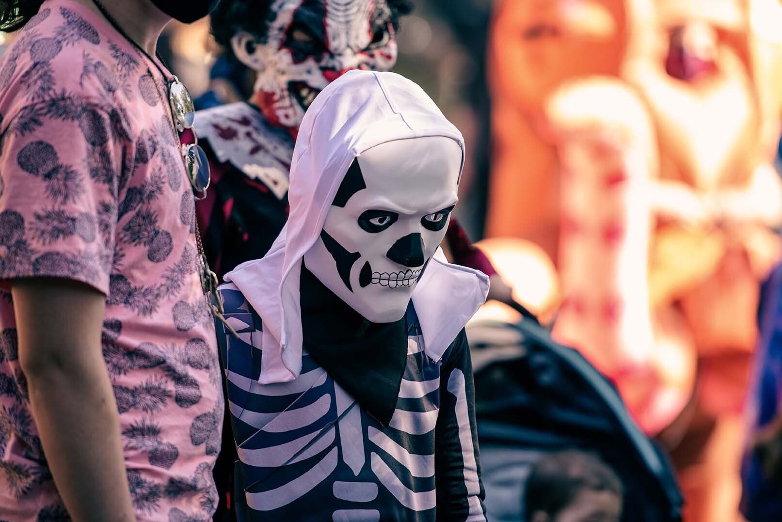 A child in a skeleton costume is standing next to a man in a pink shirt.