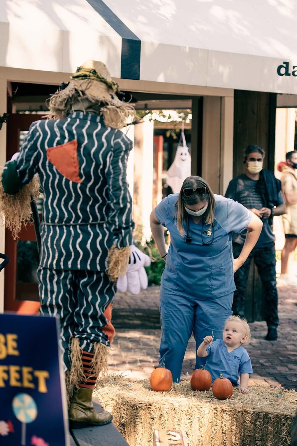 A woman in a scarecrow costume is standing next to a baby.