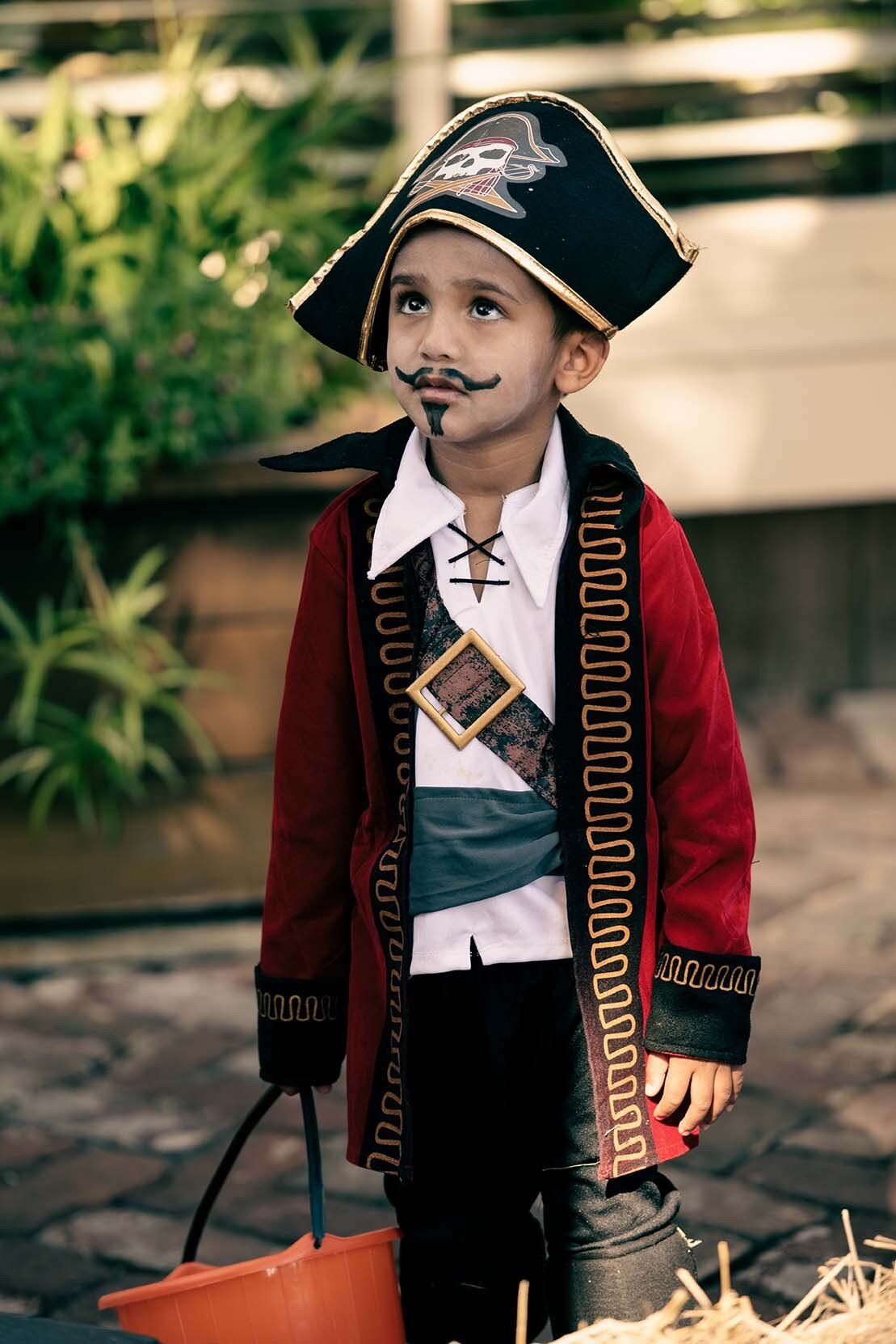 A young boy in a pirate costume is holding a trick or treat bucket.