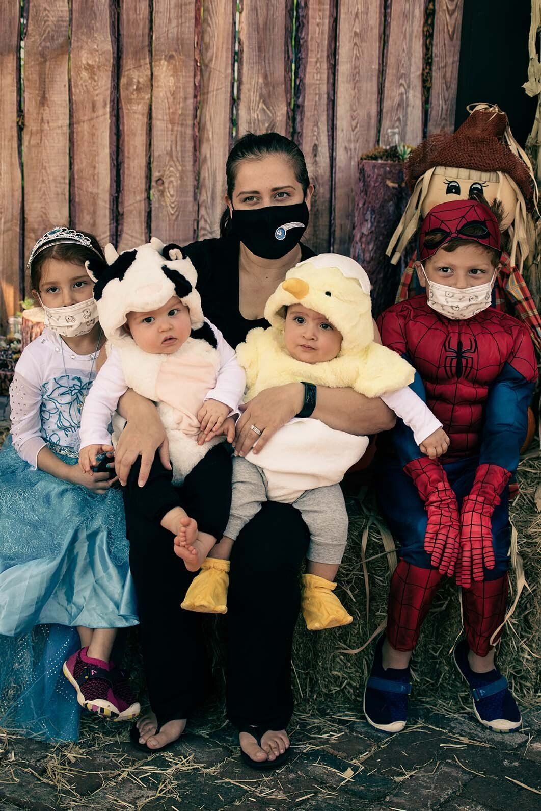 A woman is sitting on a hay bale with three children in costumes.