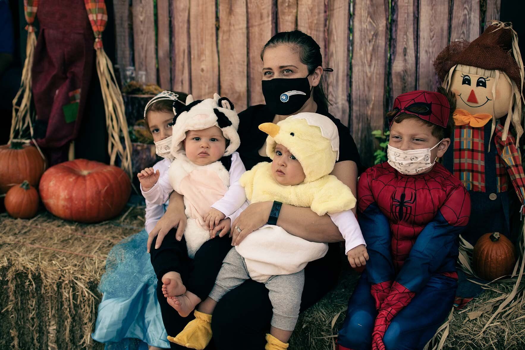 A woman is holding three babies in costumes while sitting on a bale of hay.