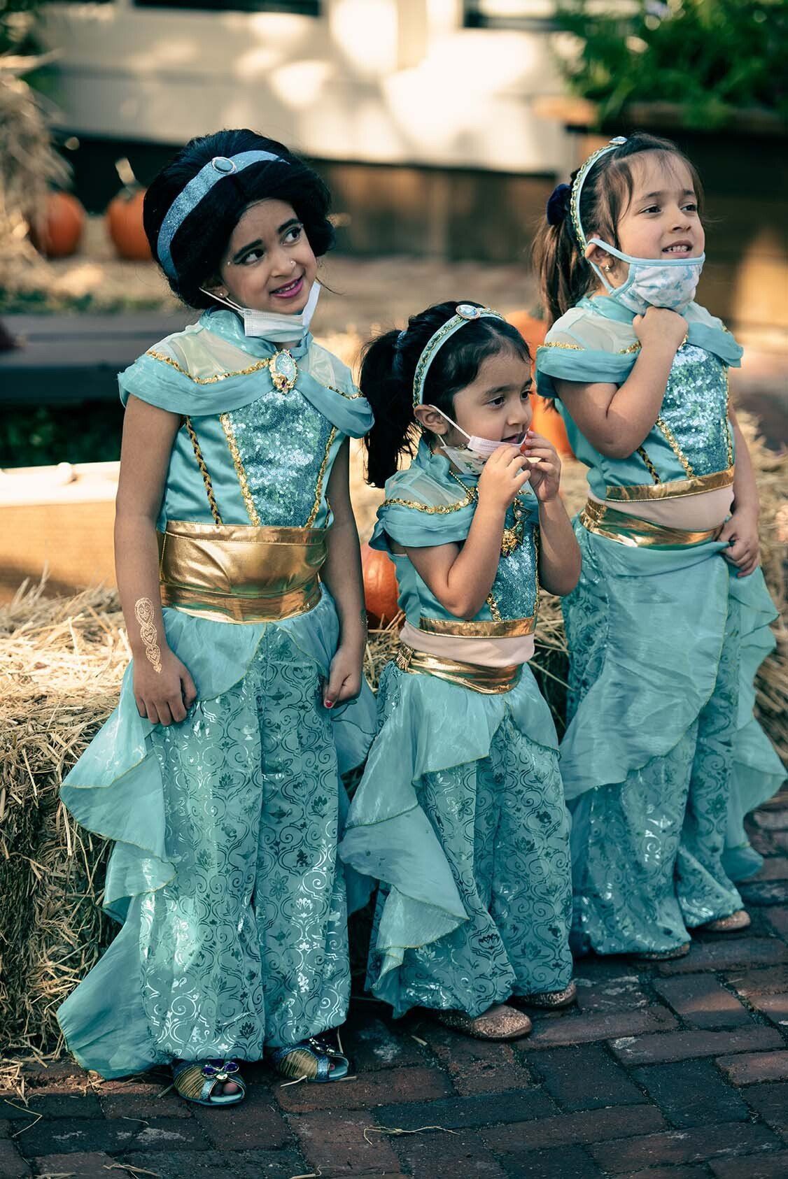 Three little girls in jasmine costumes are standing next to each other on a brick sidewalk.