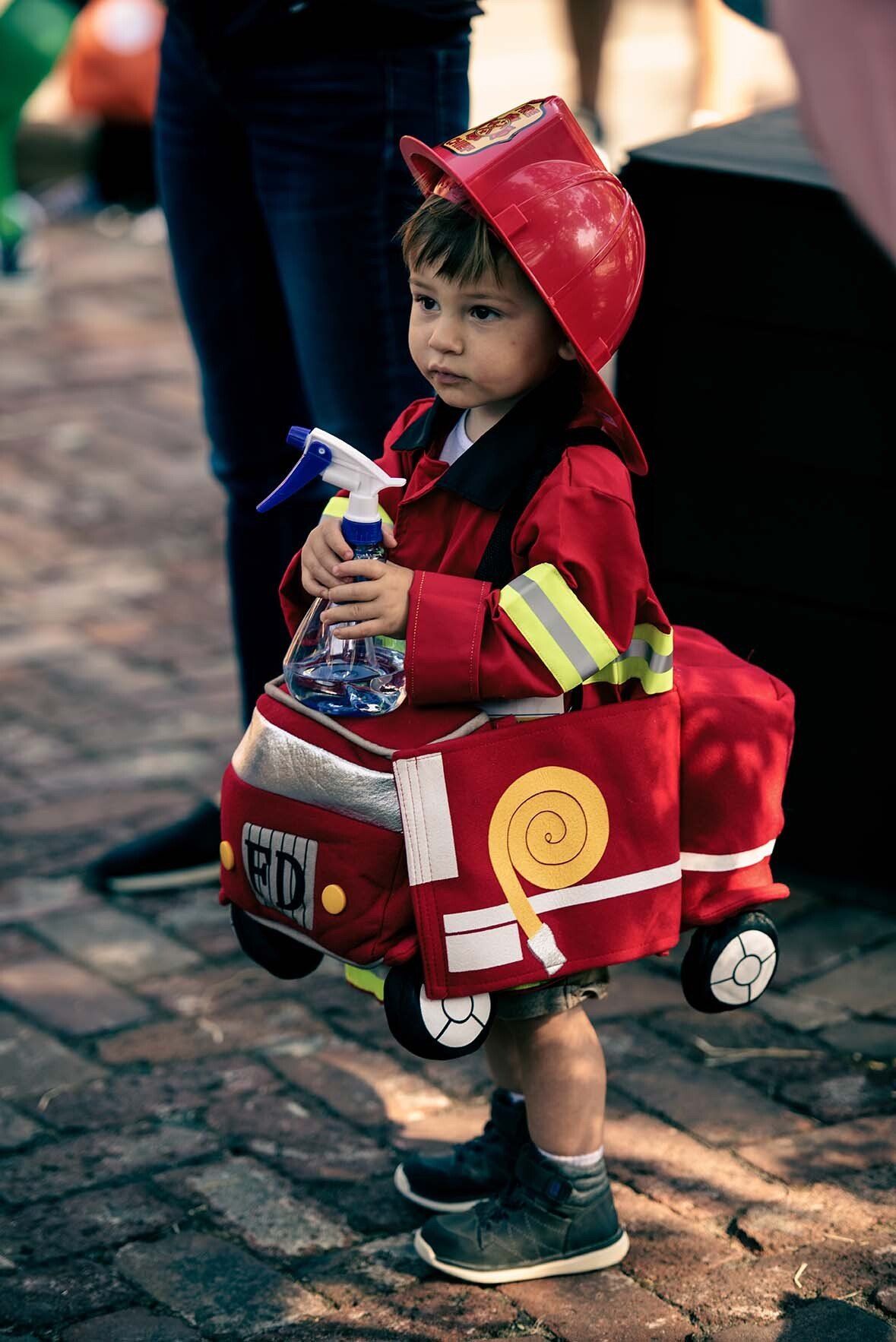 A little boy in a fireman costume is holding a spray bottle.