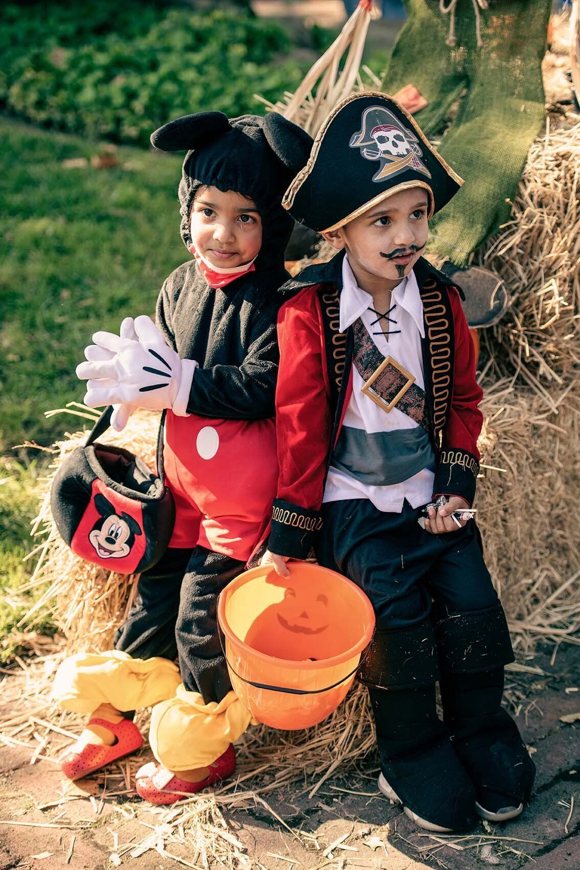 Two children in halloween costumes are sitting next to each other on a hay bale.