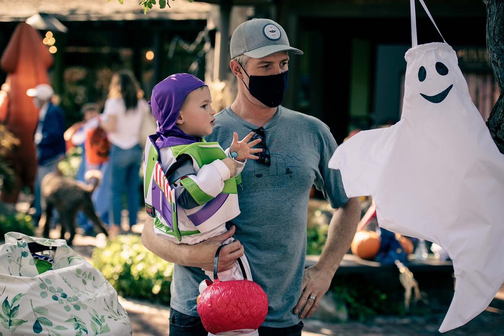 A man wearing a mask is holding a baby in a buzz lightyear costume.