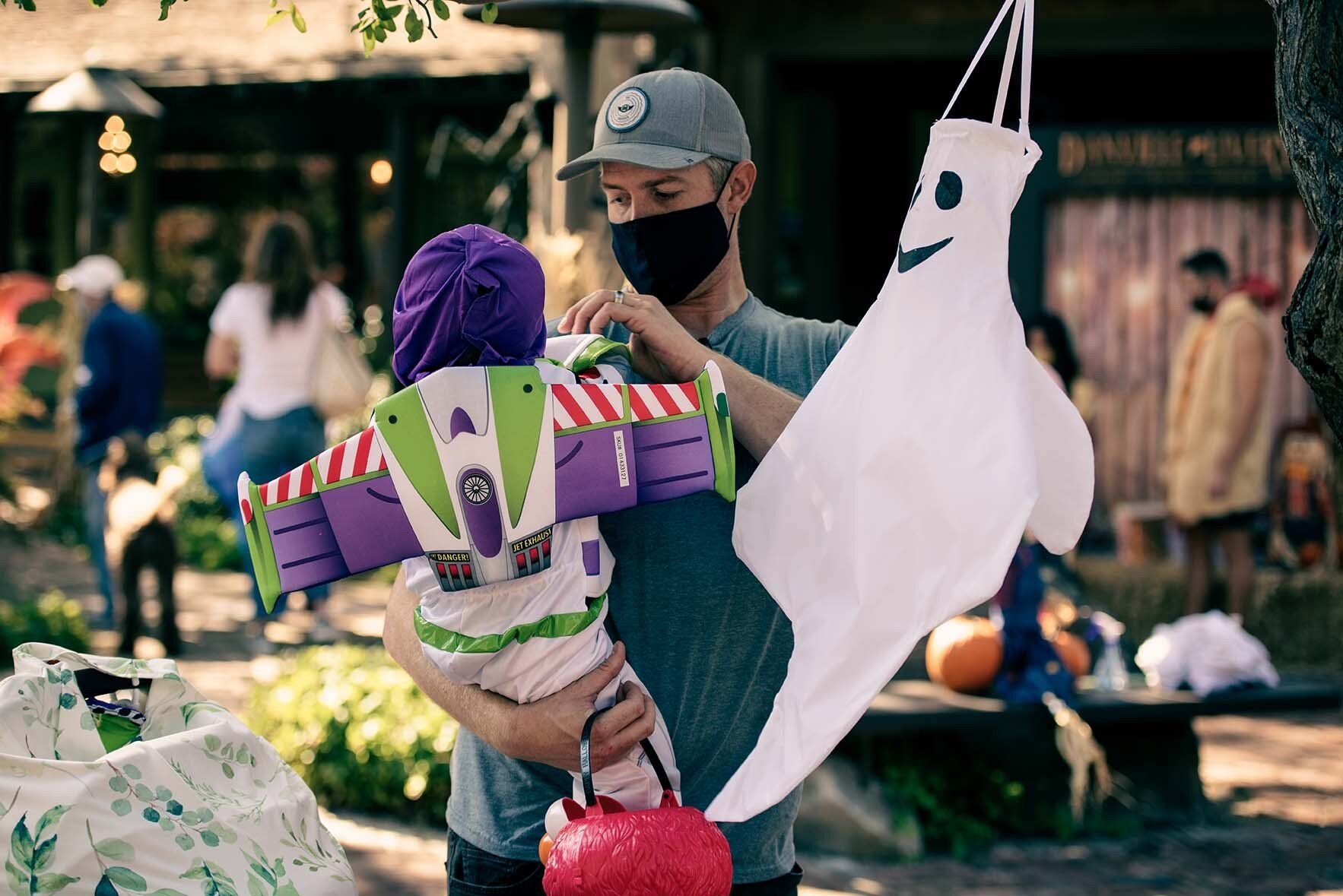 A man is holding a baby dressed as buzz lightyear and a ghost.