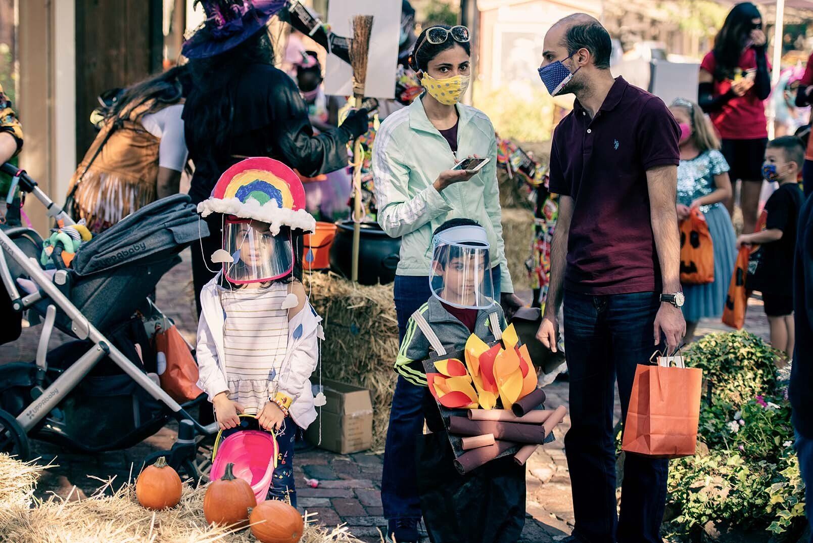A group of people wearing face masks are standing around a pumpkin patch.