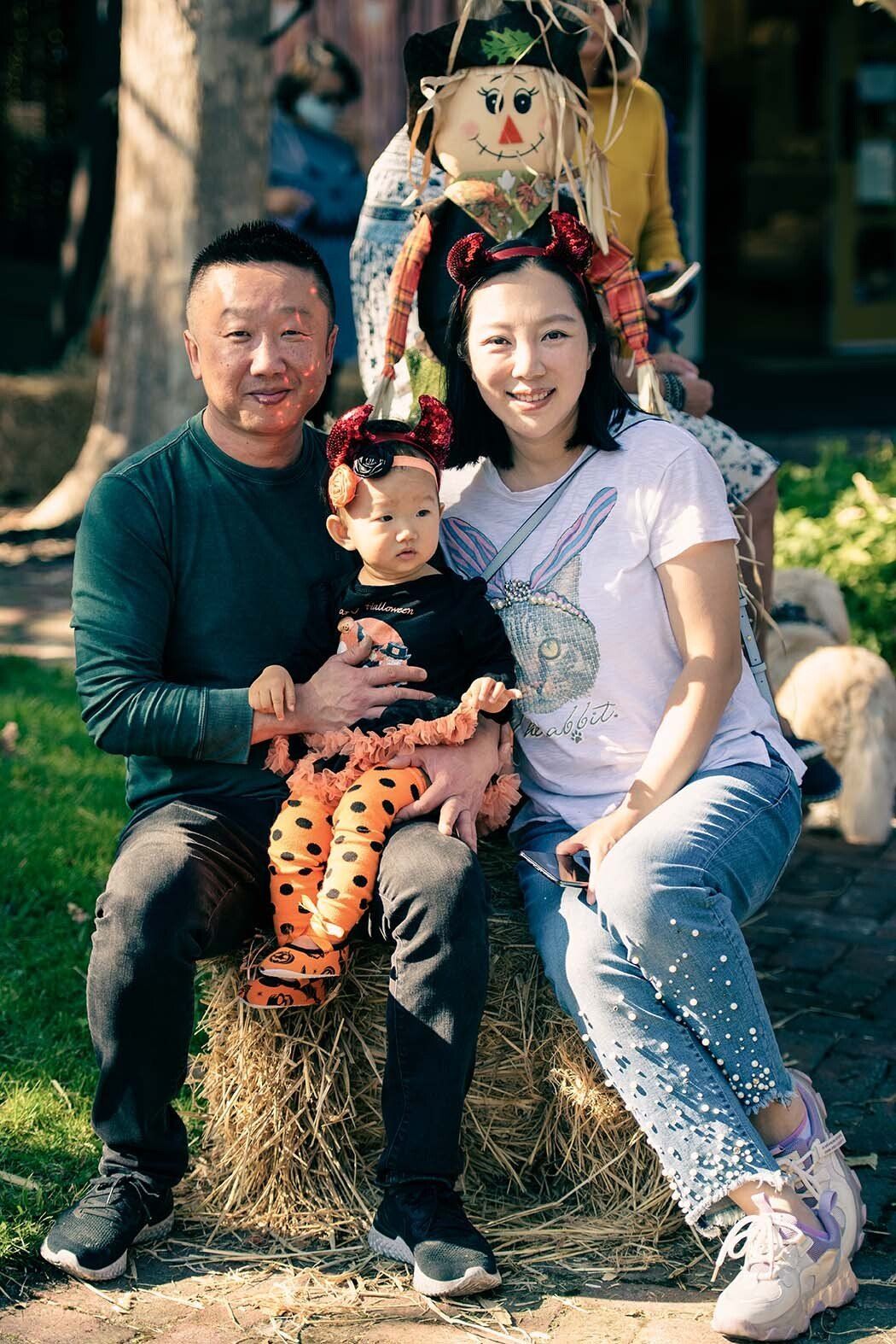 A family is posing for a picture while sitting on a bale of hay.