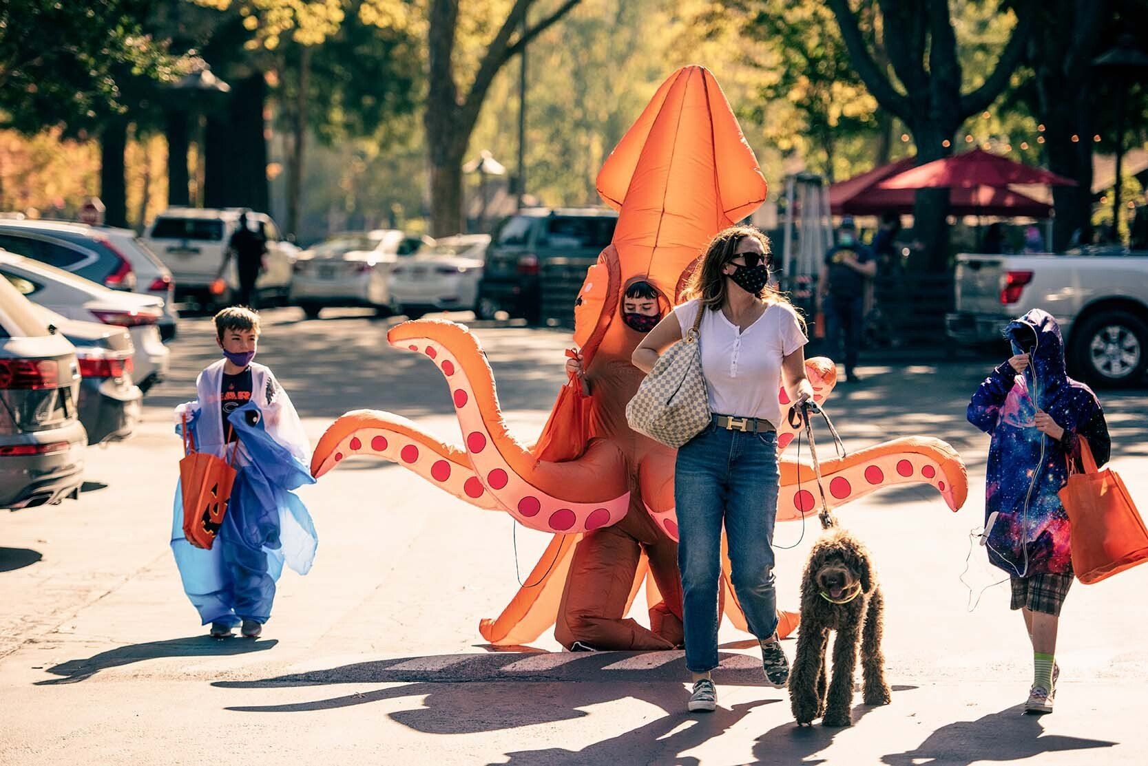 A woman is walking a dog next to a man dressed as an octopus.