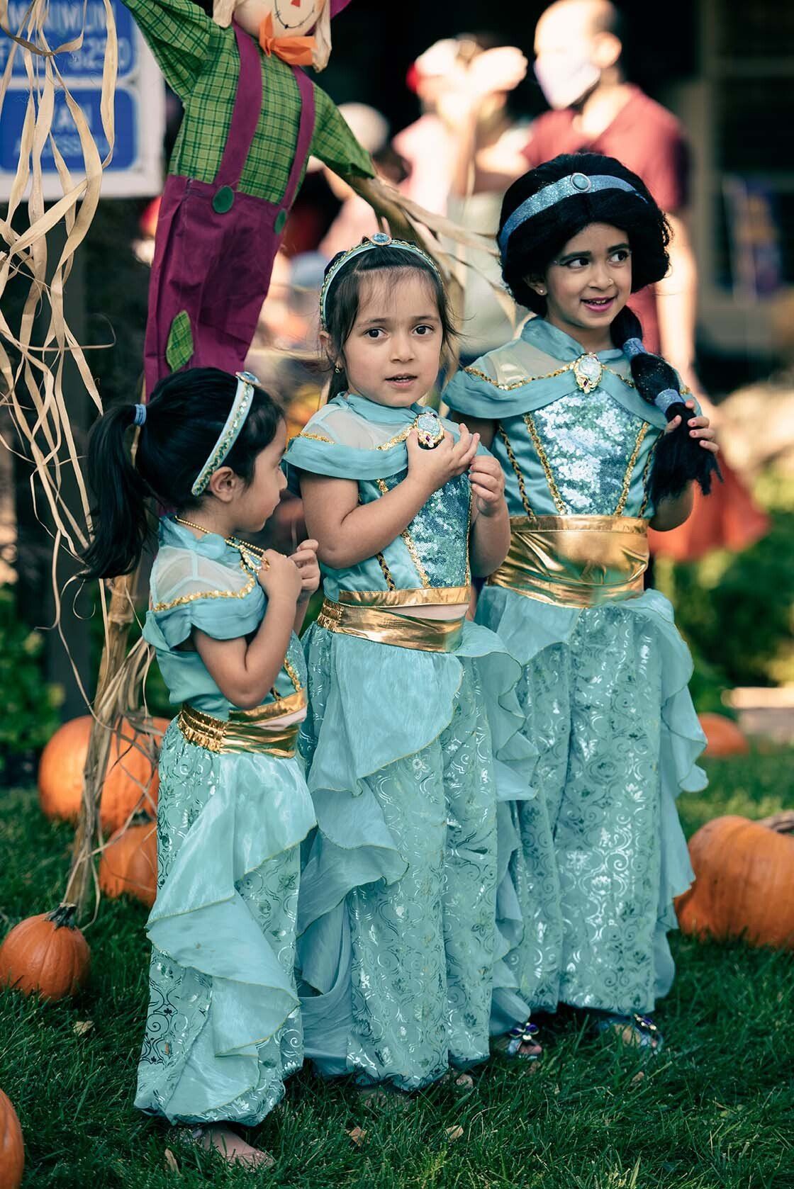 Three little girls dressed as jasmine are standing next to each other in front of pumpkins.