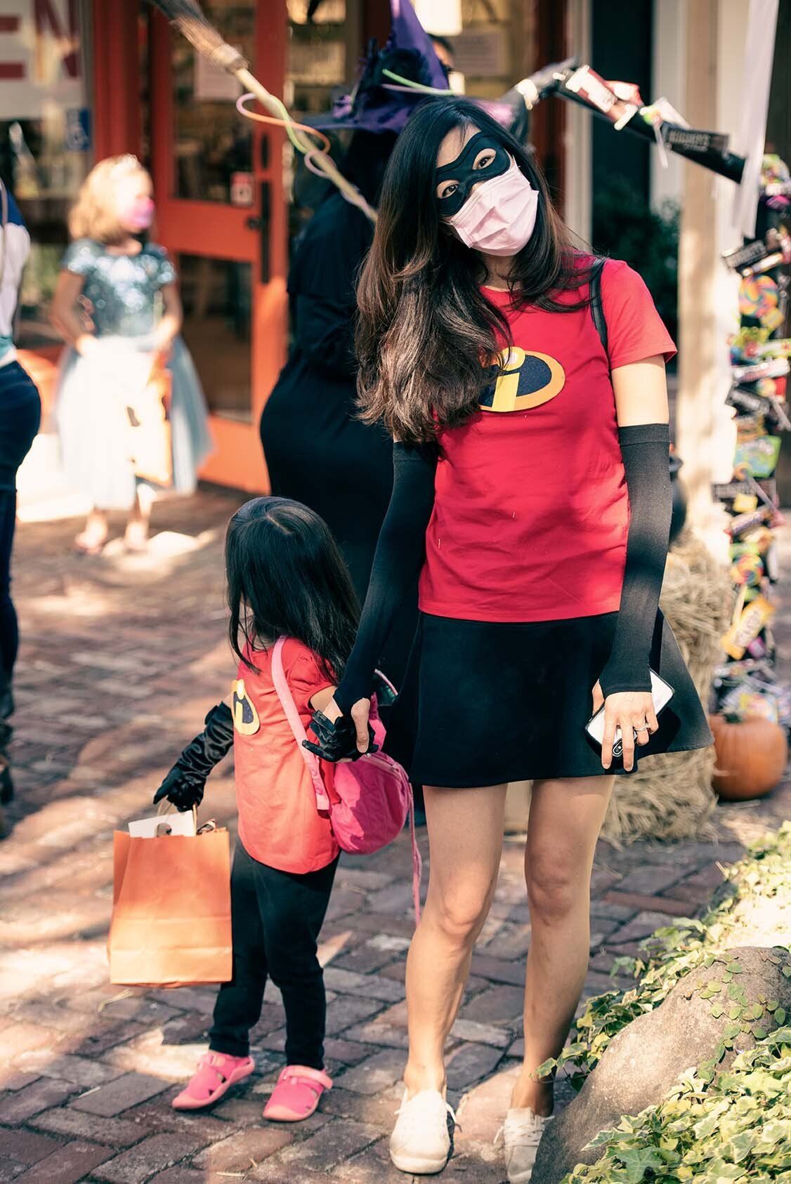 A woman in a superhero costume is holding a little girl 's hand.