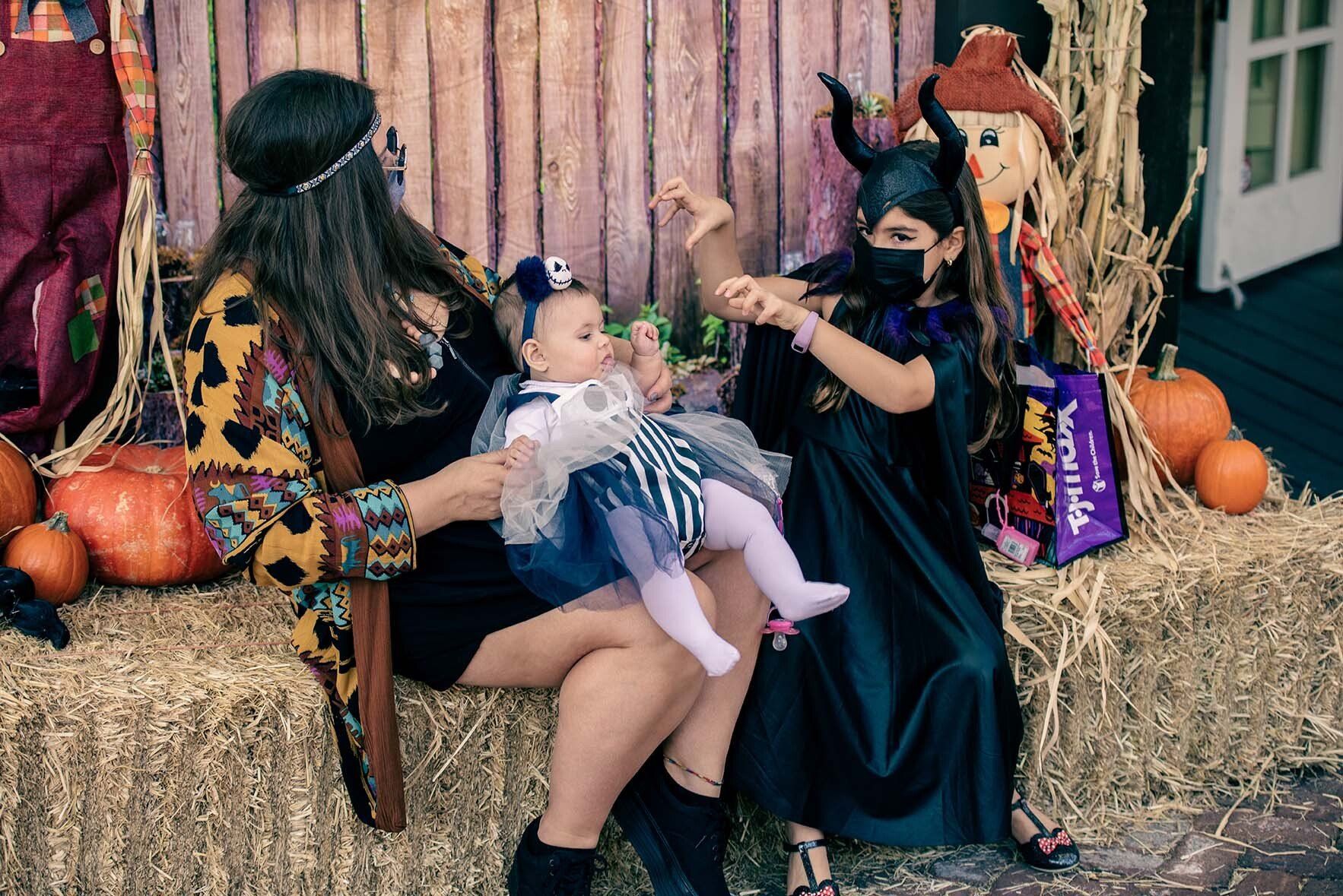 A woman is holding a baby while sitting on a hay bale.