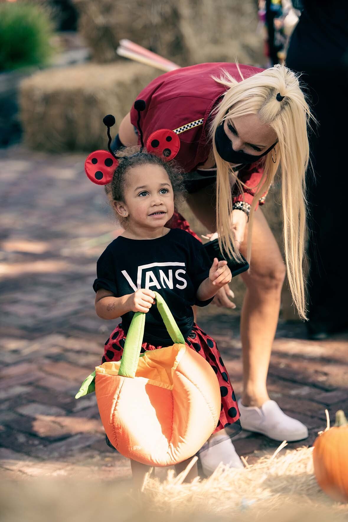 A woman is helping a little girl dressed in a ladybug costume.