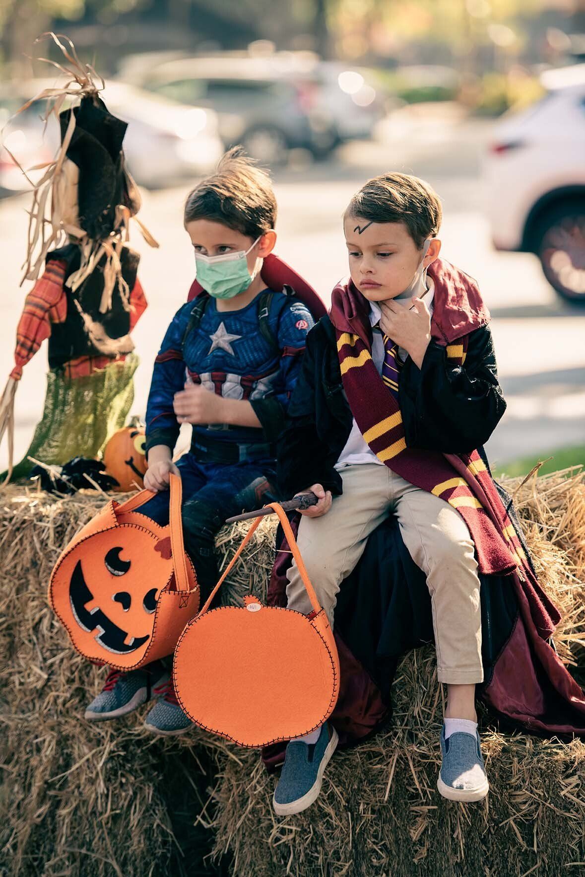 Two young boys in halloween costumes are sitting on a bale of hay.