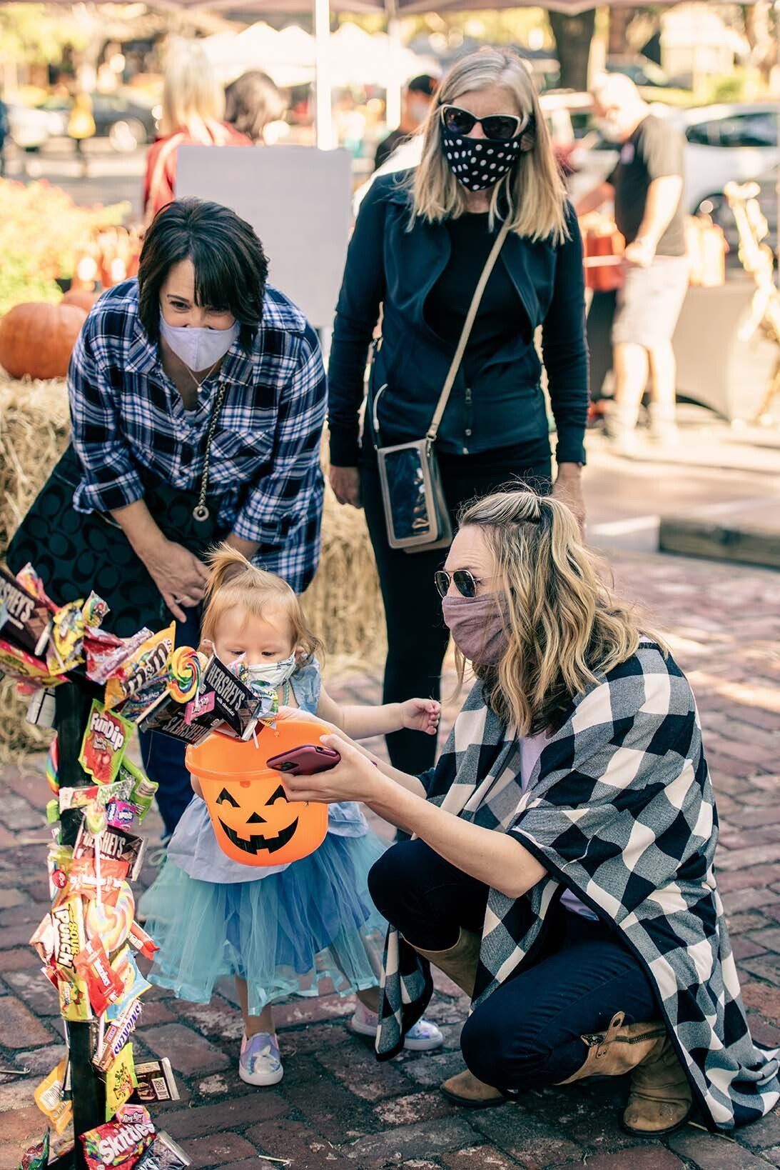 A woman is kneeling down next to a little girl wearing a mask.