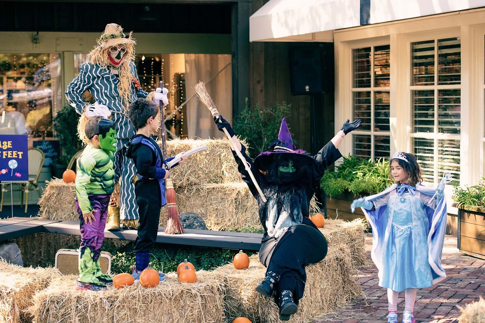 A group of children dressed in halloween costumes are standing on hay bales.