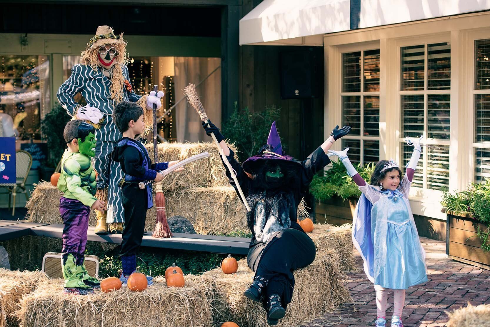 A group of children dressed in halloween costumes are standing around hay bales.