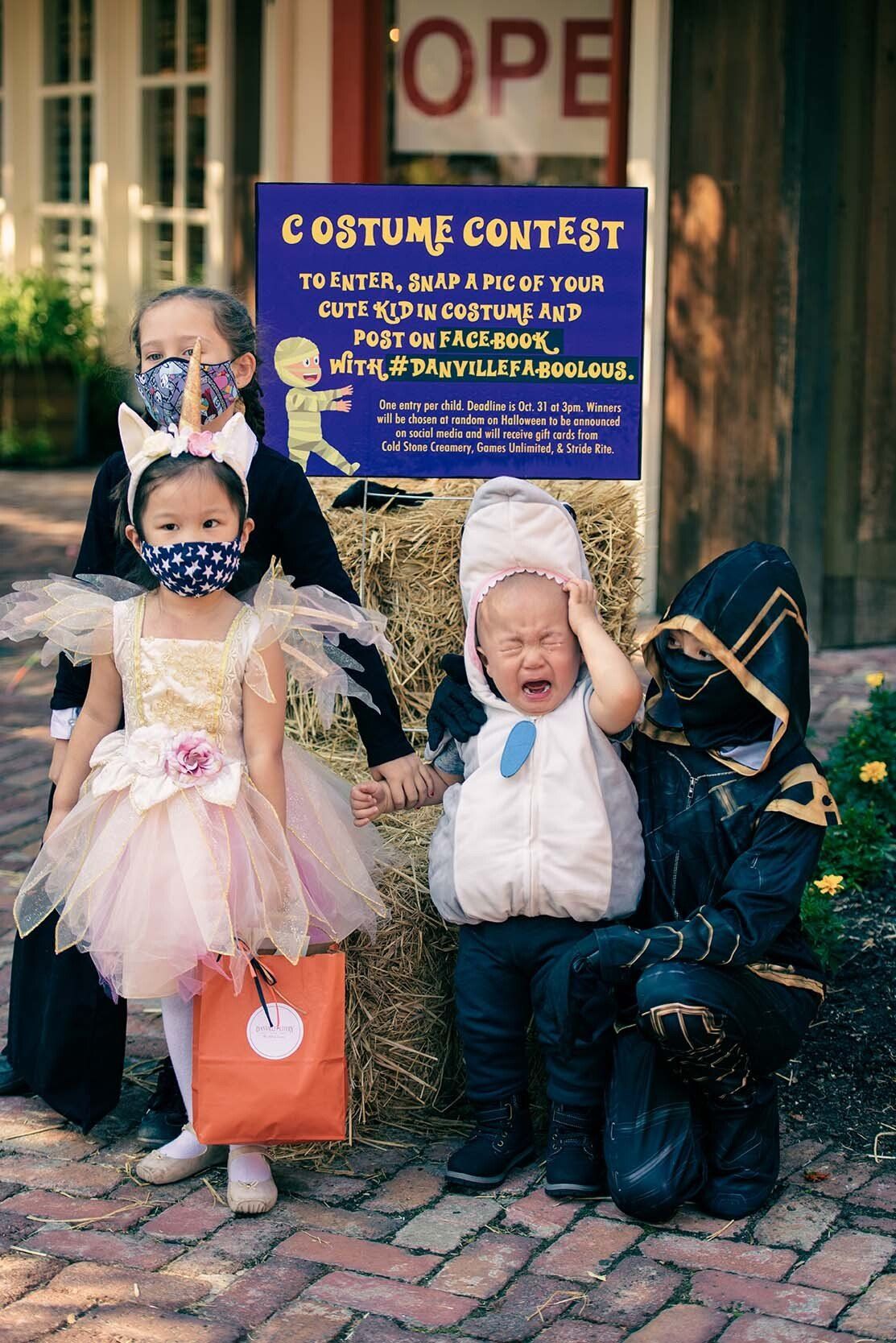 A group of children in costumes are standing next to each other on a brick sidewalk.
