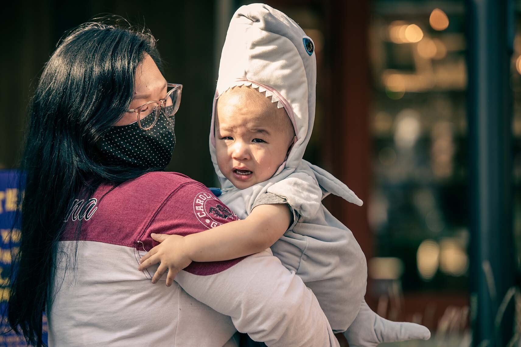 A woman is holding a baby in a shark costume.