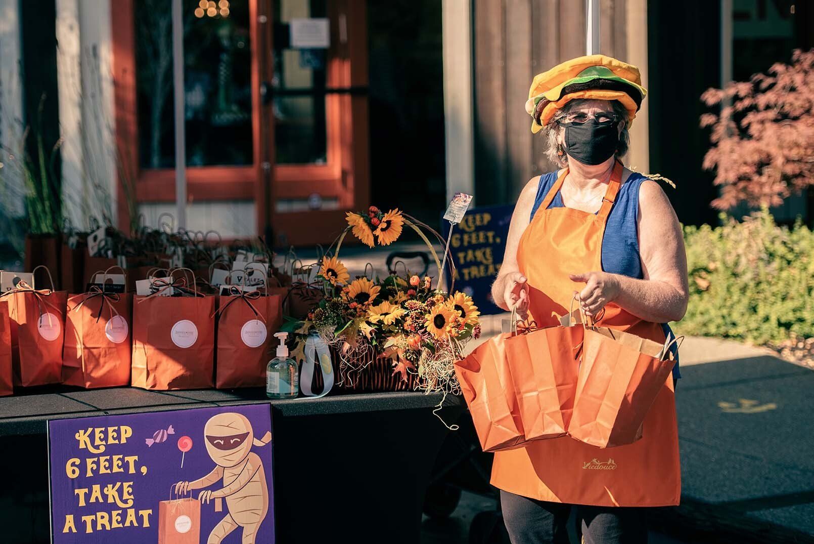 A woman wearing a mask is standing in front of a table with bags and flowers.