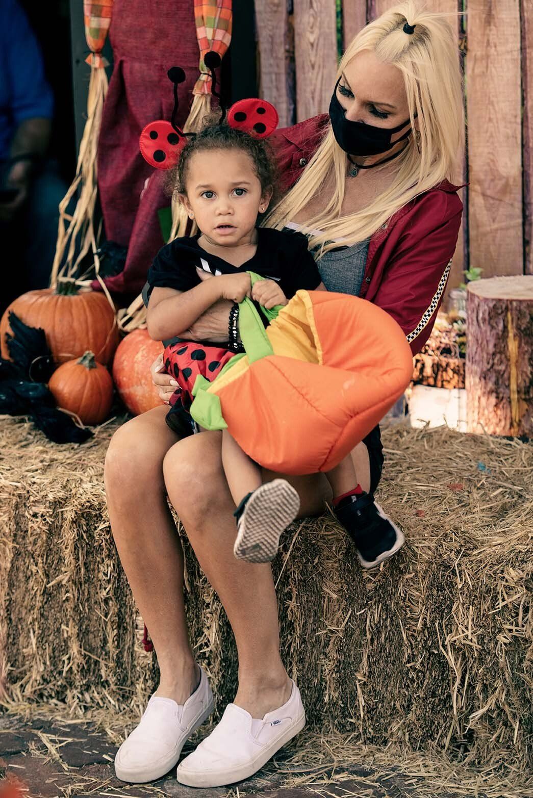 A woman is holding a little girl in her arms while sitting on a bale of hay.