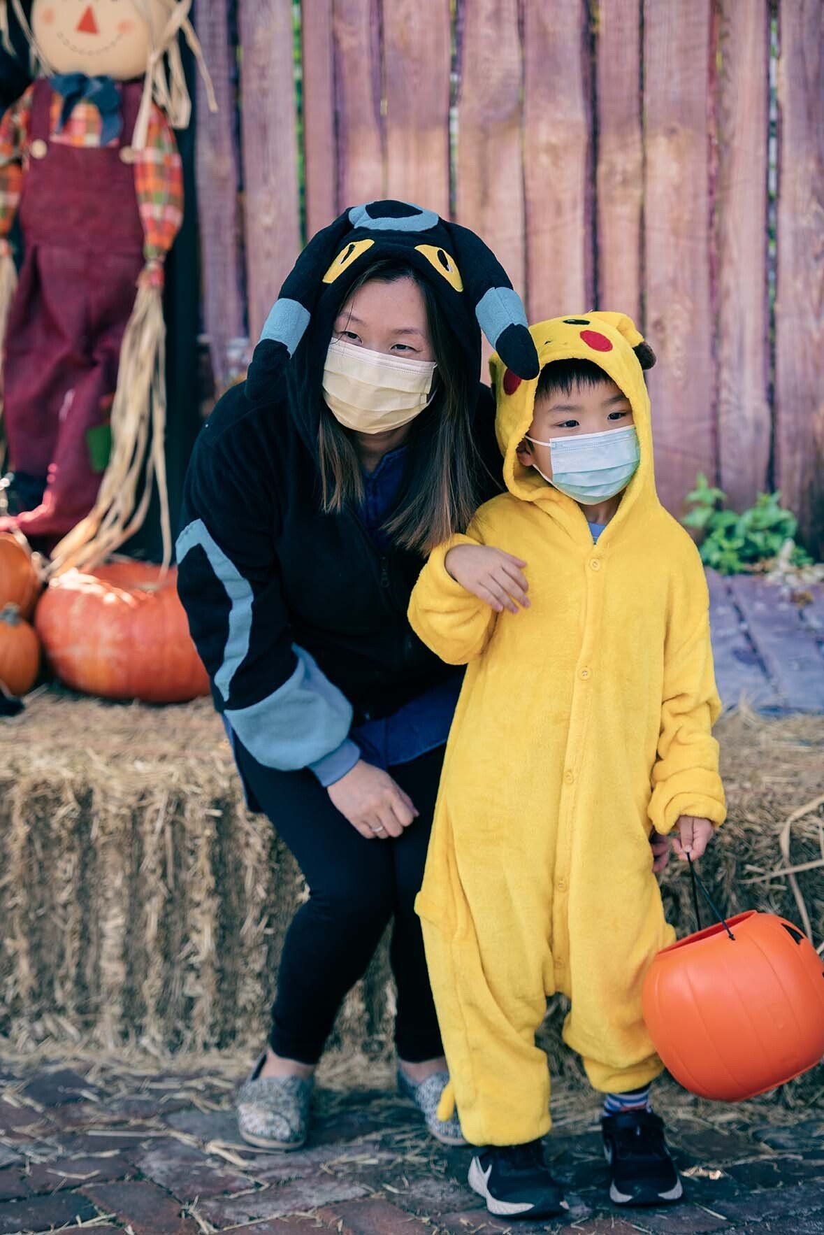 A woman is standing next to a child in a pikachu costume.