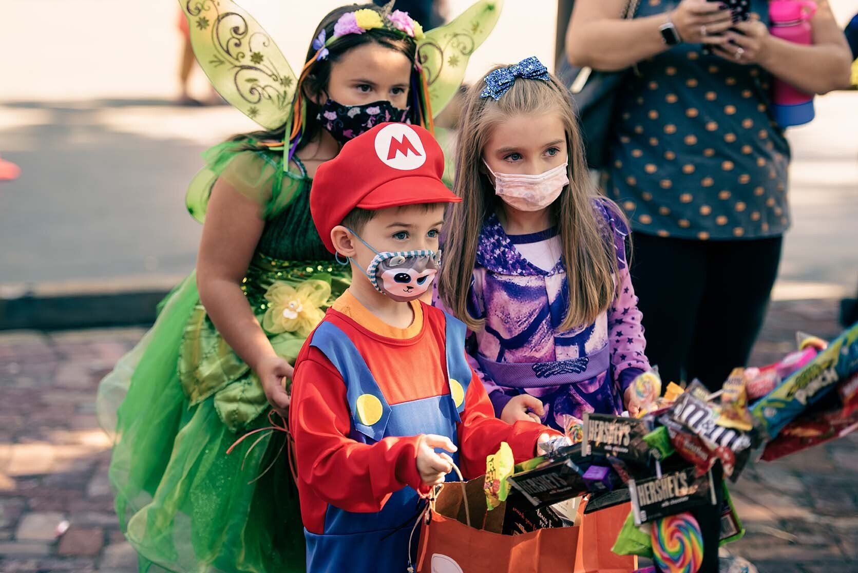 A group of children wearing masks and costumes are trick or treating.