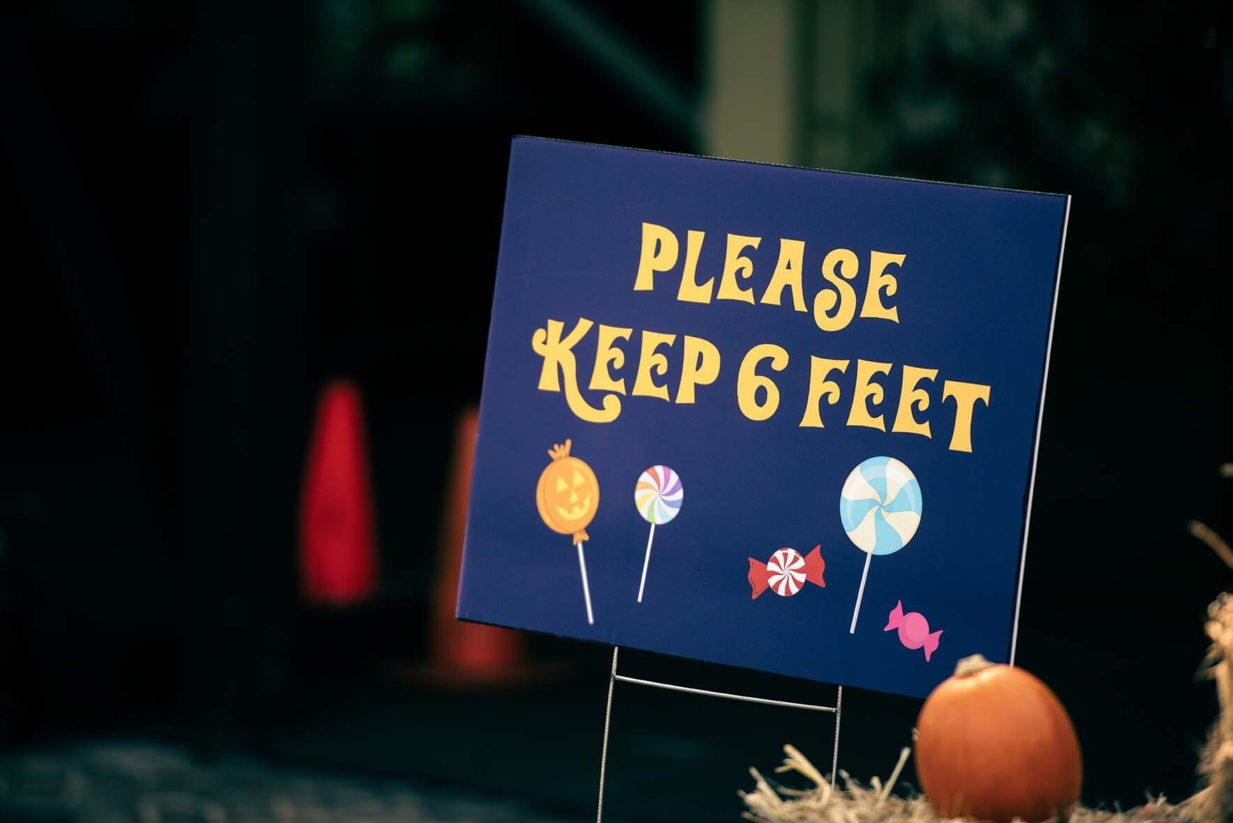 A sign that says please keep 6 feet next to a pumpkin