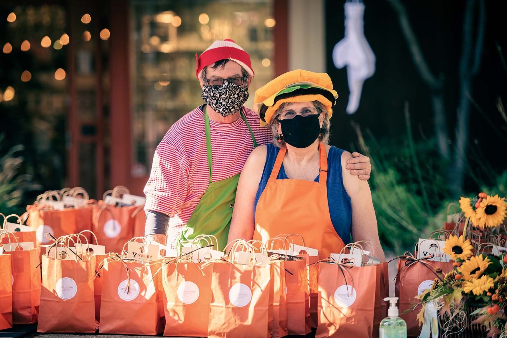 A man and a woman wearing masks are standing in front of a table filled with bags.