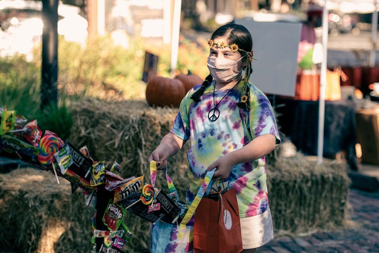 A young girl wearing a face mask is holding a bag of candy.