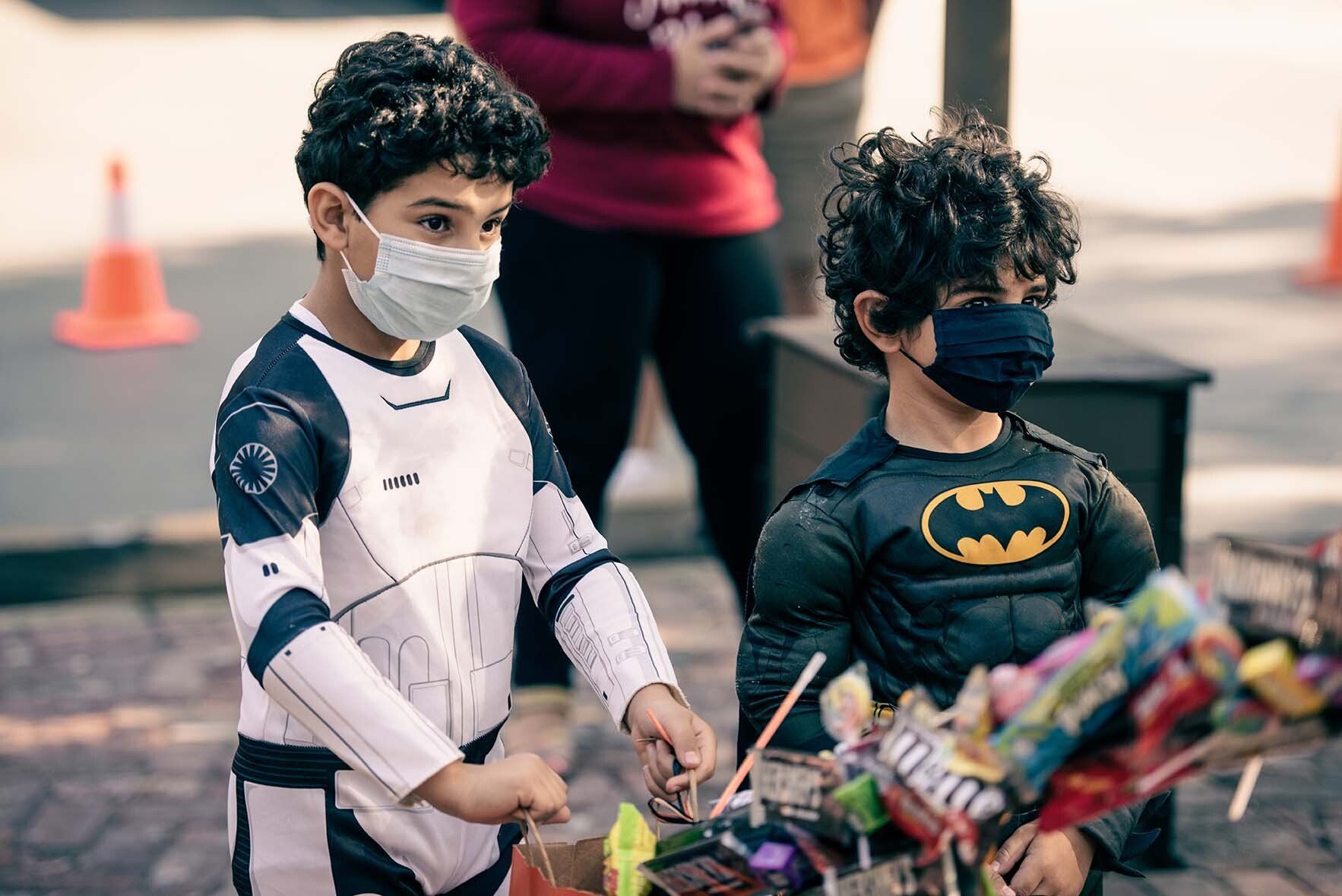 Two young boys wearing masks are standing next to each other on a sidewalk.