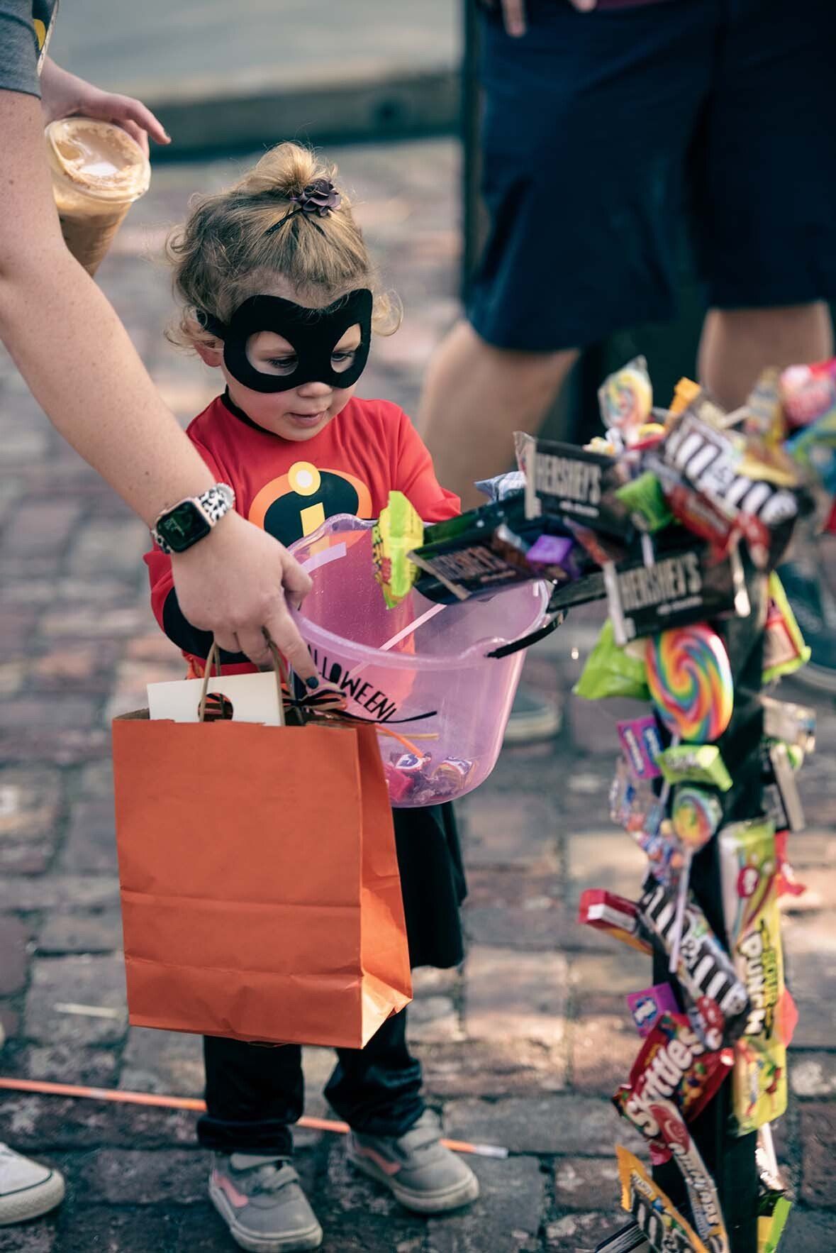 A little girl in a superhero costume is holding a bag of candy.