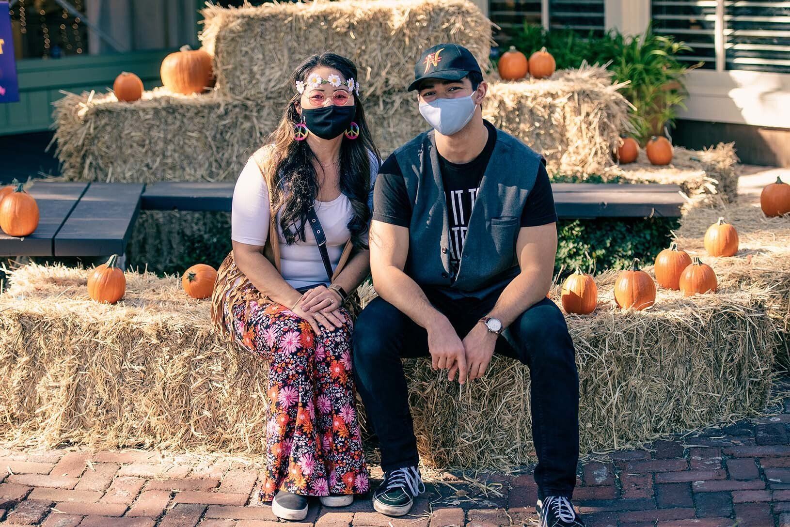 A man and a woman wearing masks are sitting on hay bales.
