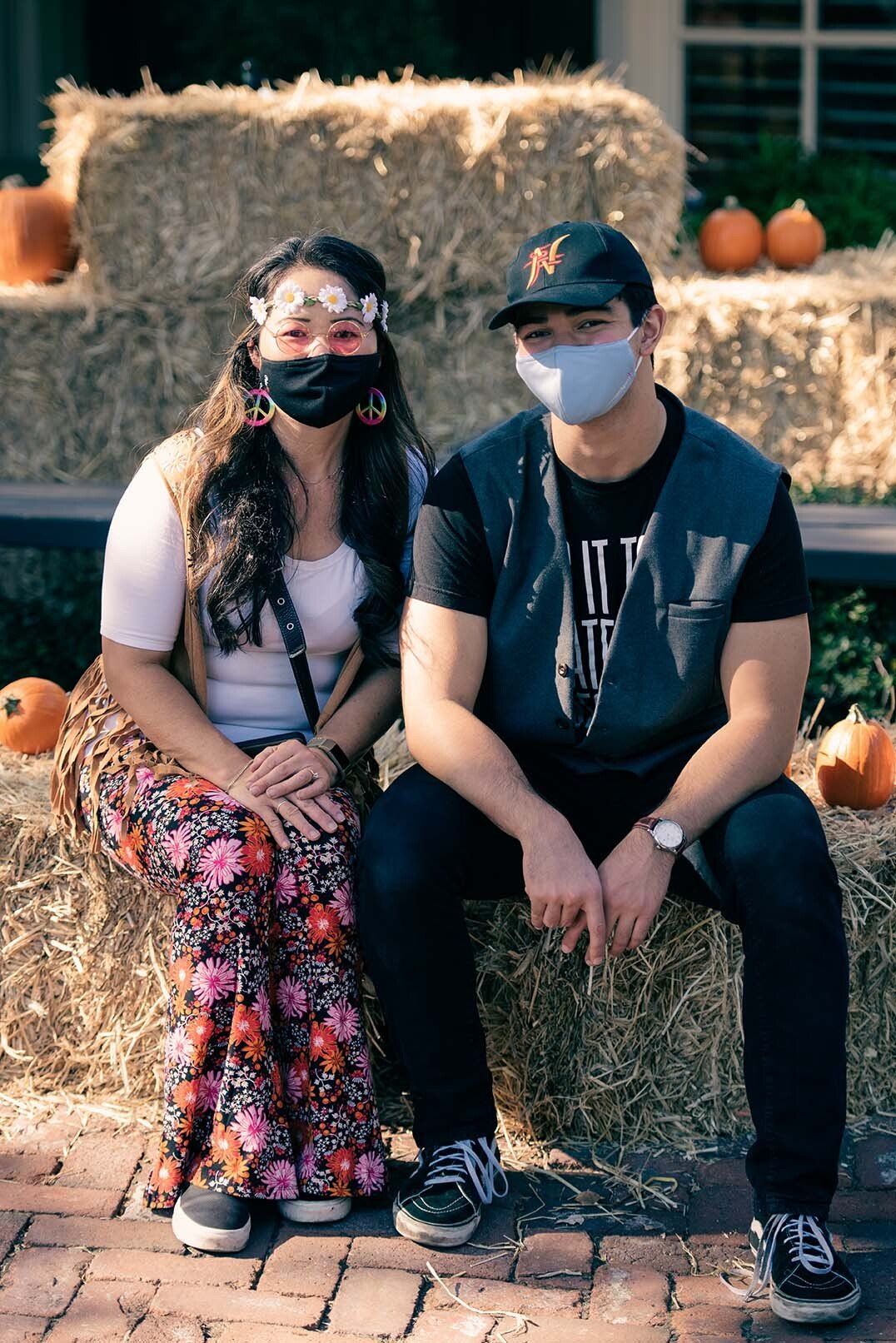 A man and a woman wearing face masks are sitting on a hay bale.