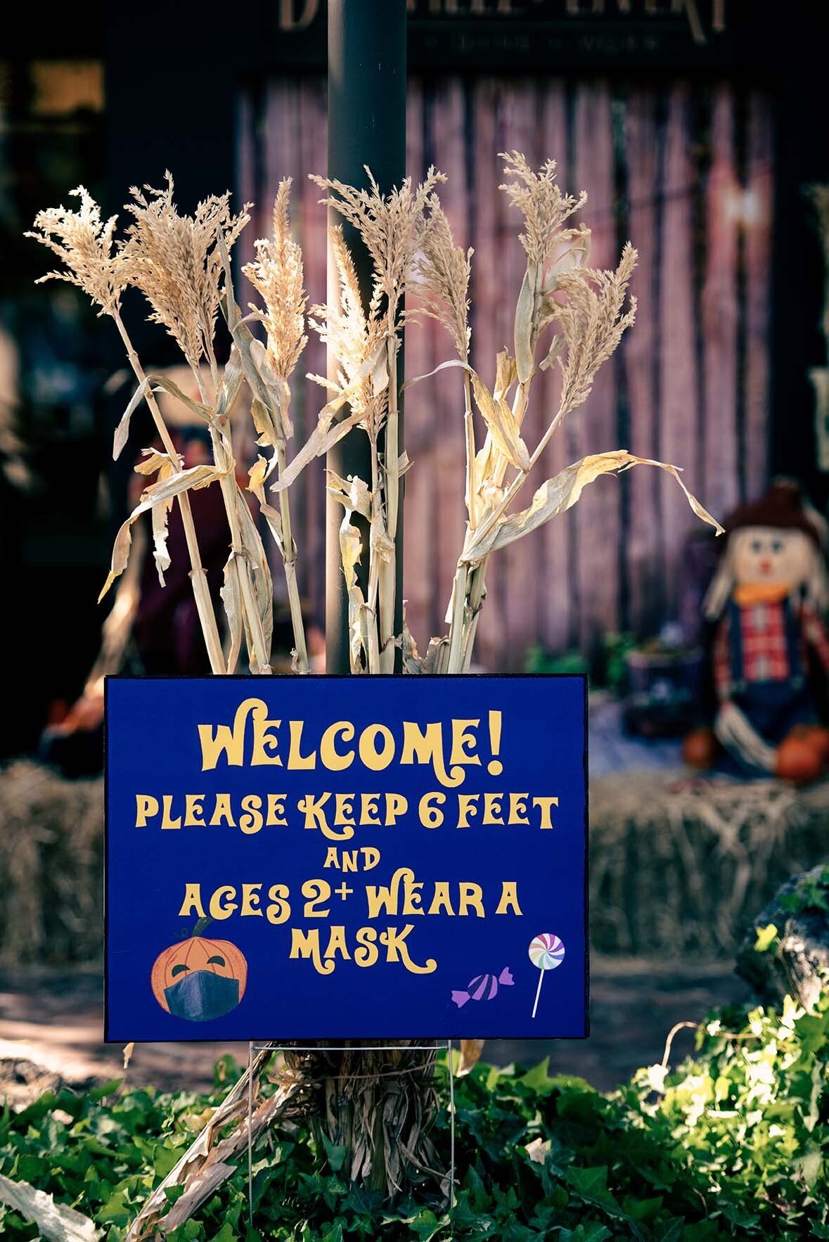 A blue sign that says `` welcome please keep 6 feet and ages 2 wear a mask ''