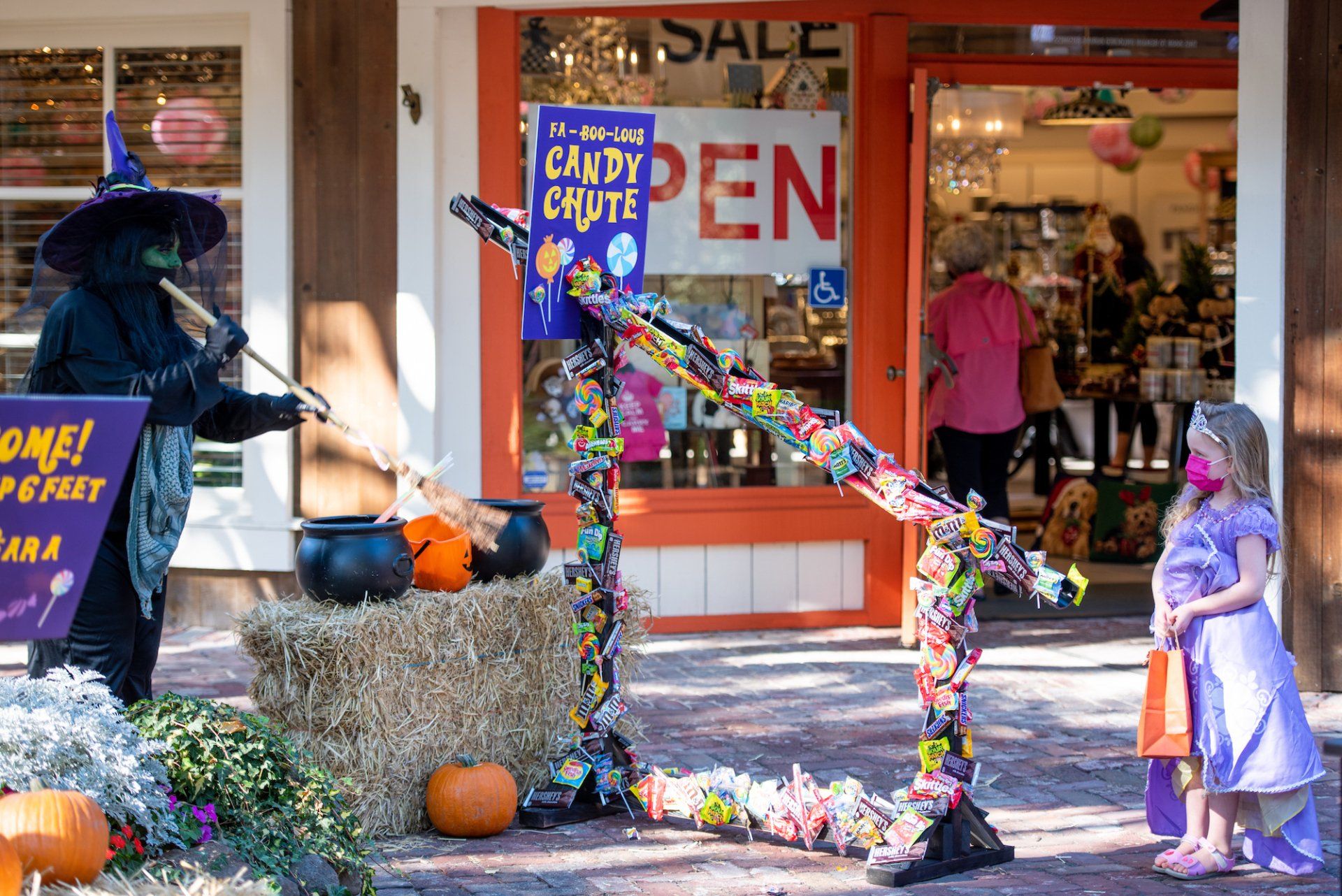 A woman in a witch costume is standing in front of a store.