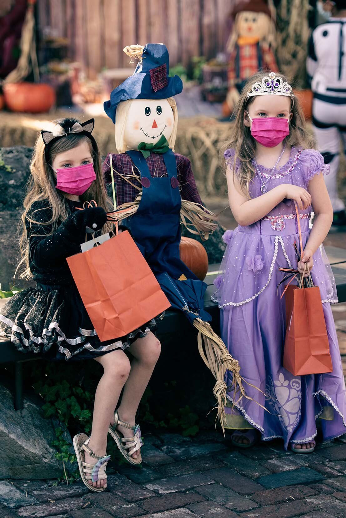Three little girls in halloween costumes wearing face masks.