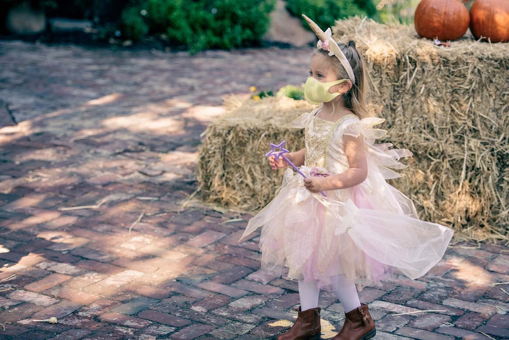 A little girl in a unicorn costume is wearing a mask.
