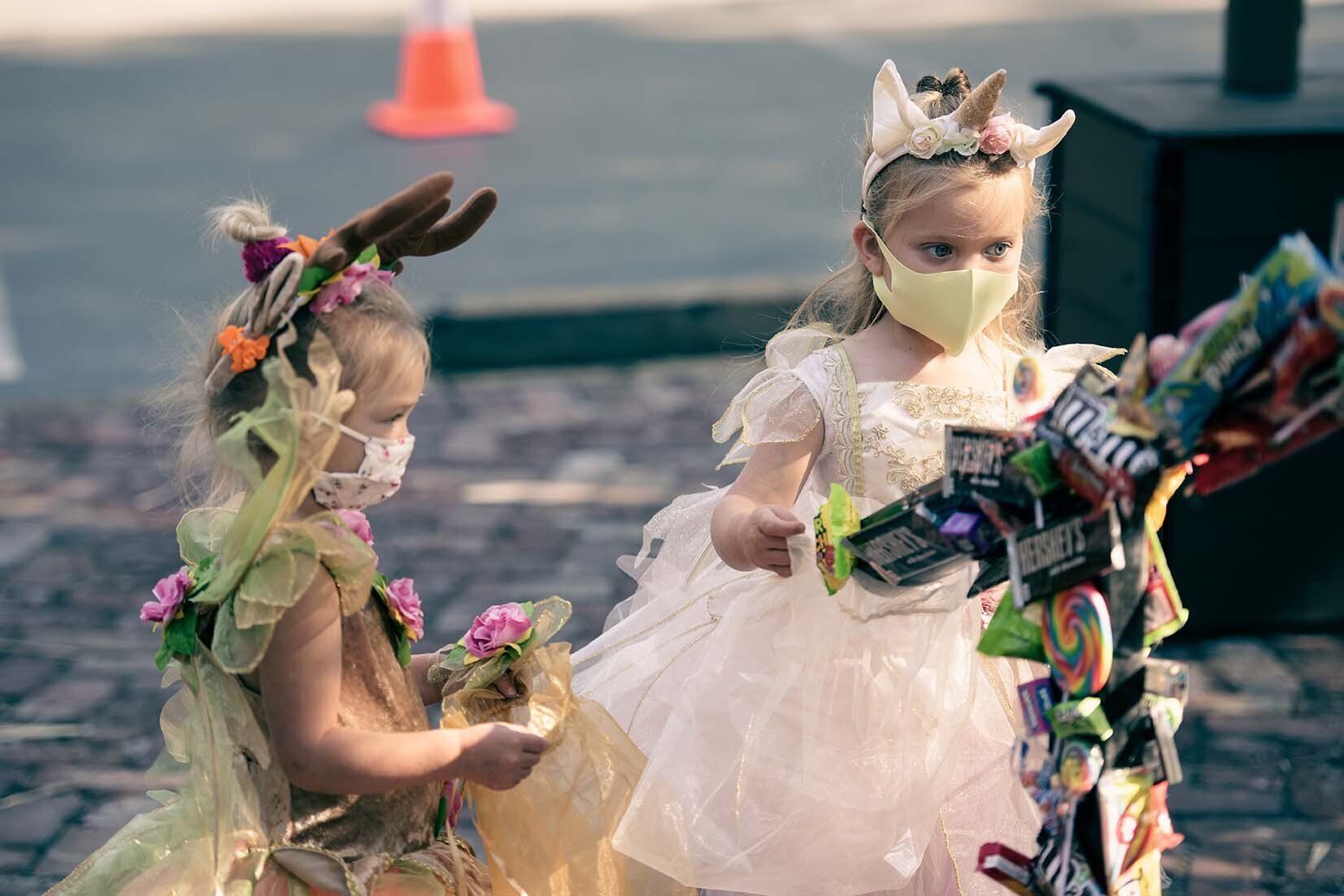 Two little girls wearing masks are standing next to each other on a sidewalk.