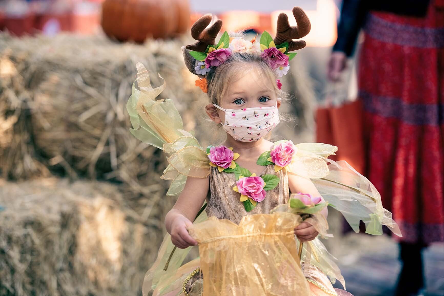 A little girl in a fairy costume is wearing a face mask.
