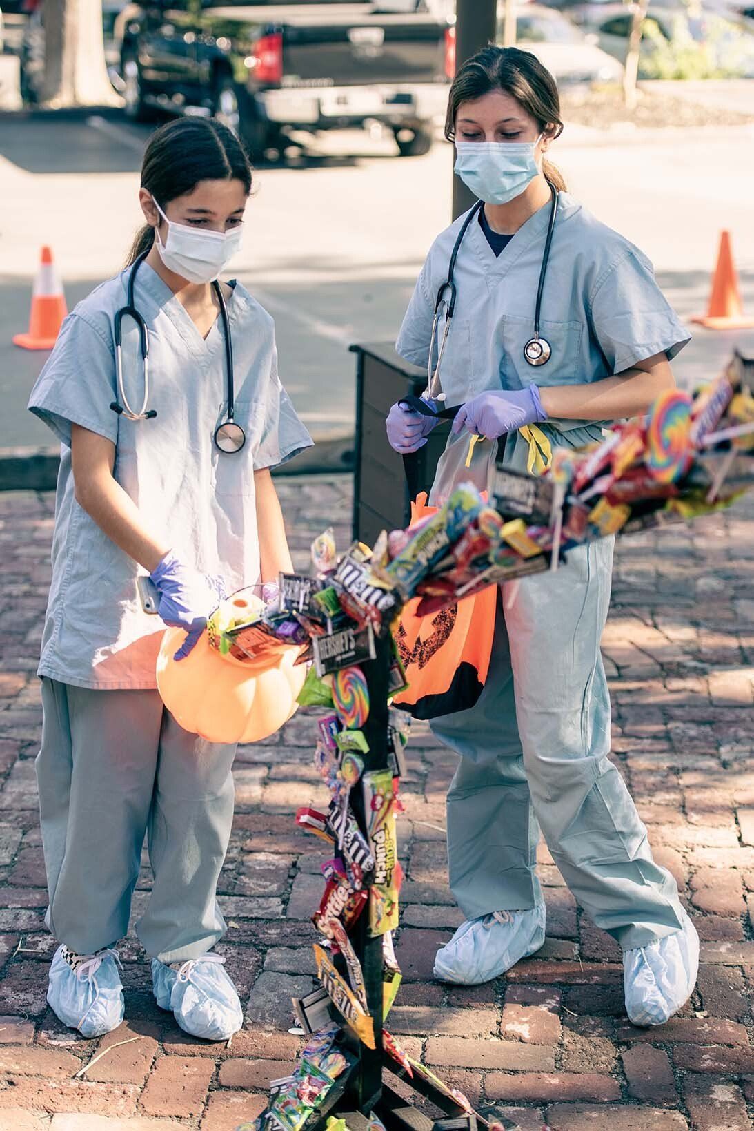 Two young girls dressed as doctors are standing next to a candy tree.