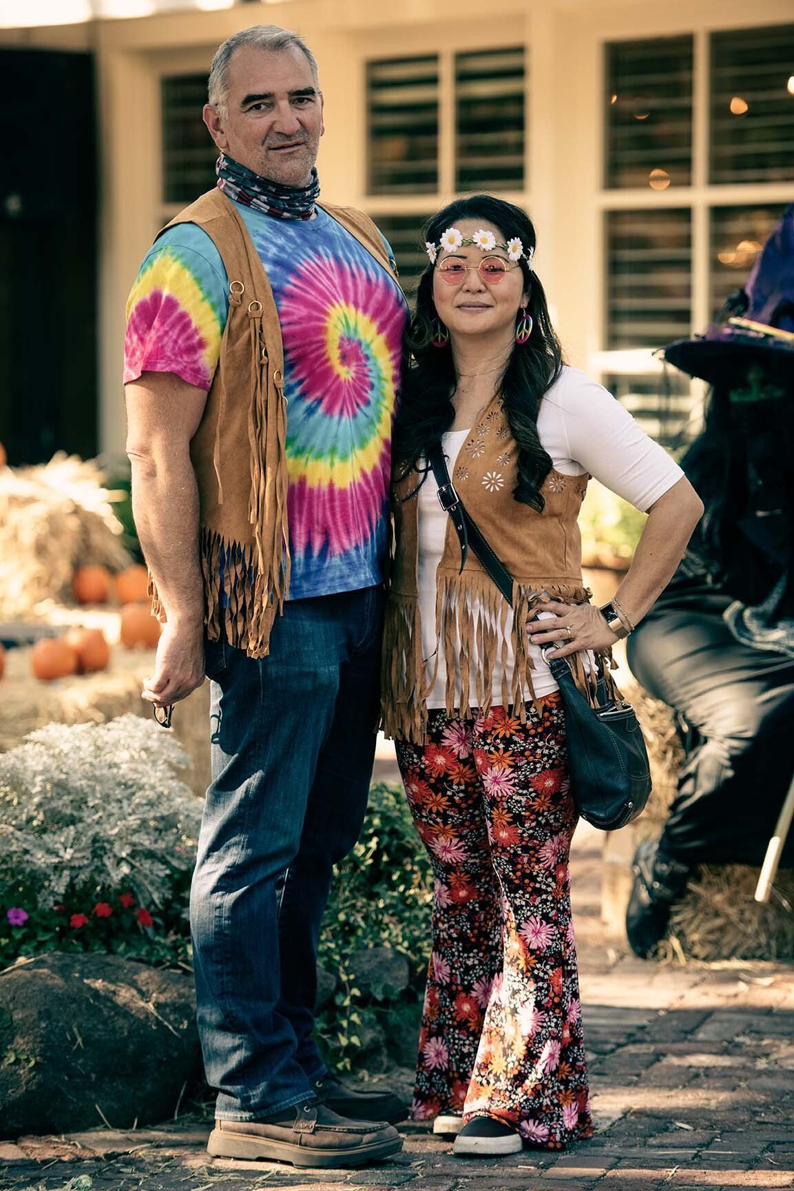 A man and a woman dressed in hippie costumes are posing for a picture.