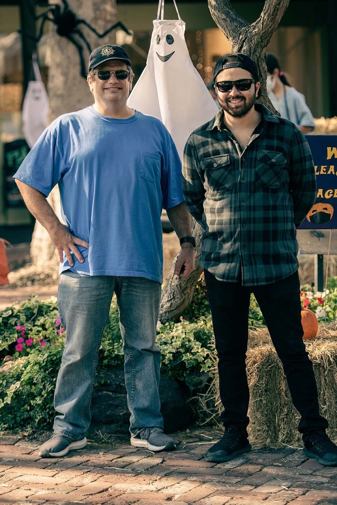 Two men are standing next to each other in front of a ghost hanging from a tree.