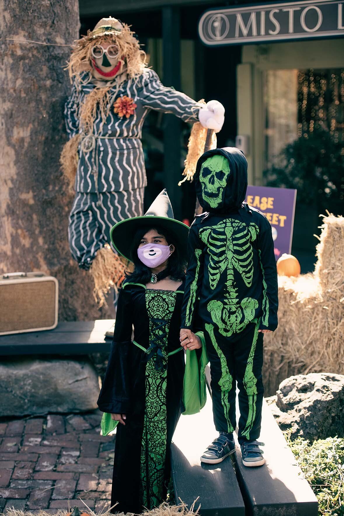 A girl in a witch costume stands next to a boy in a skeleton costume