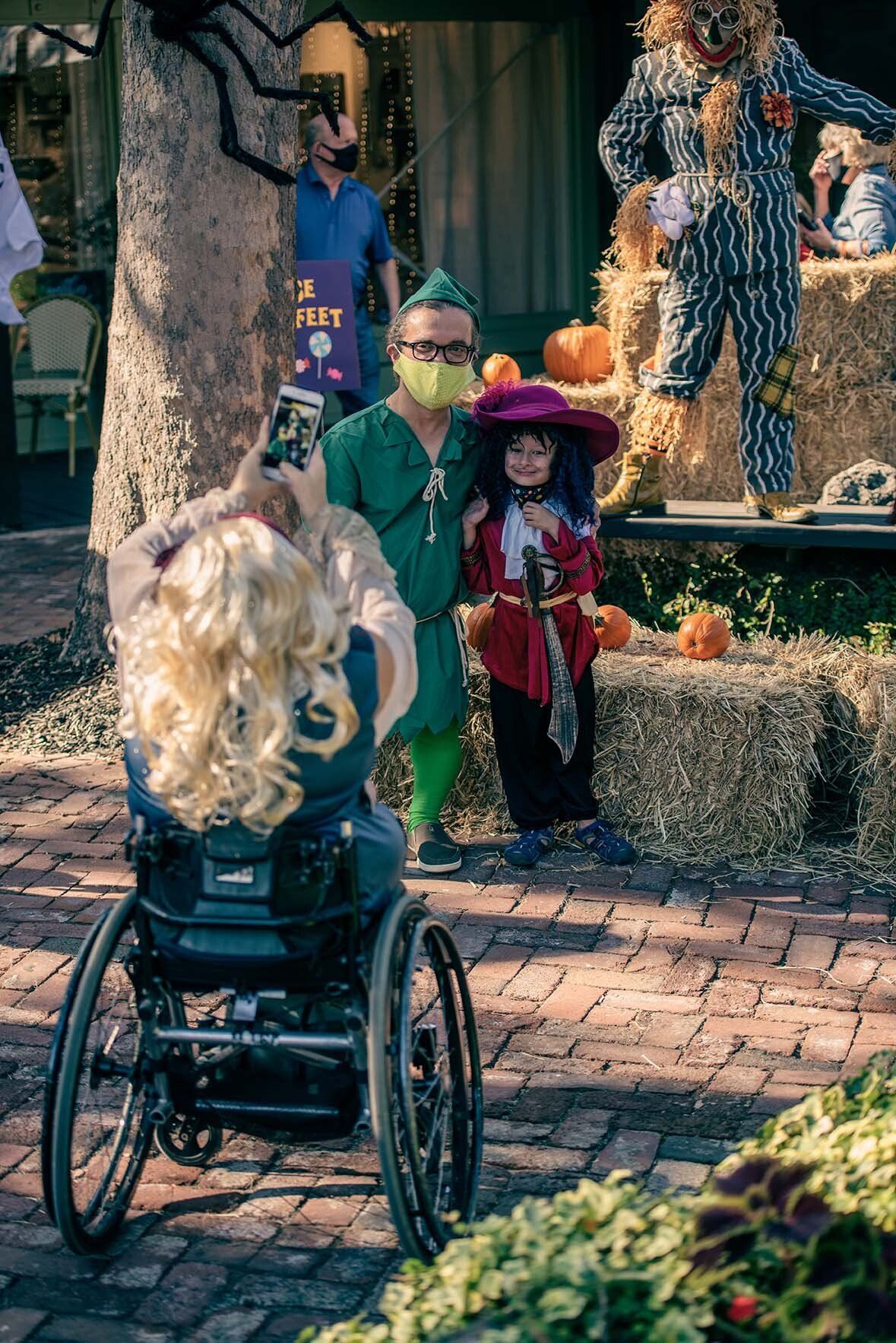 A woman in a wheelchair is standing next to a child in a halloween costume.