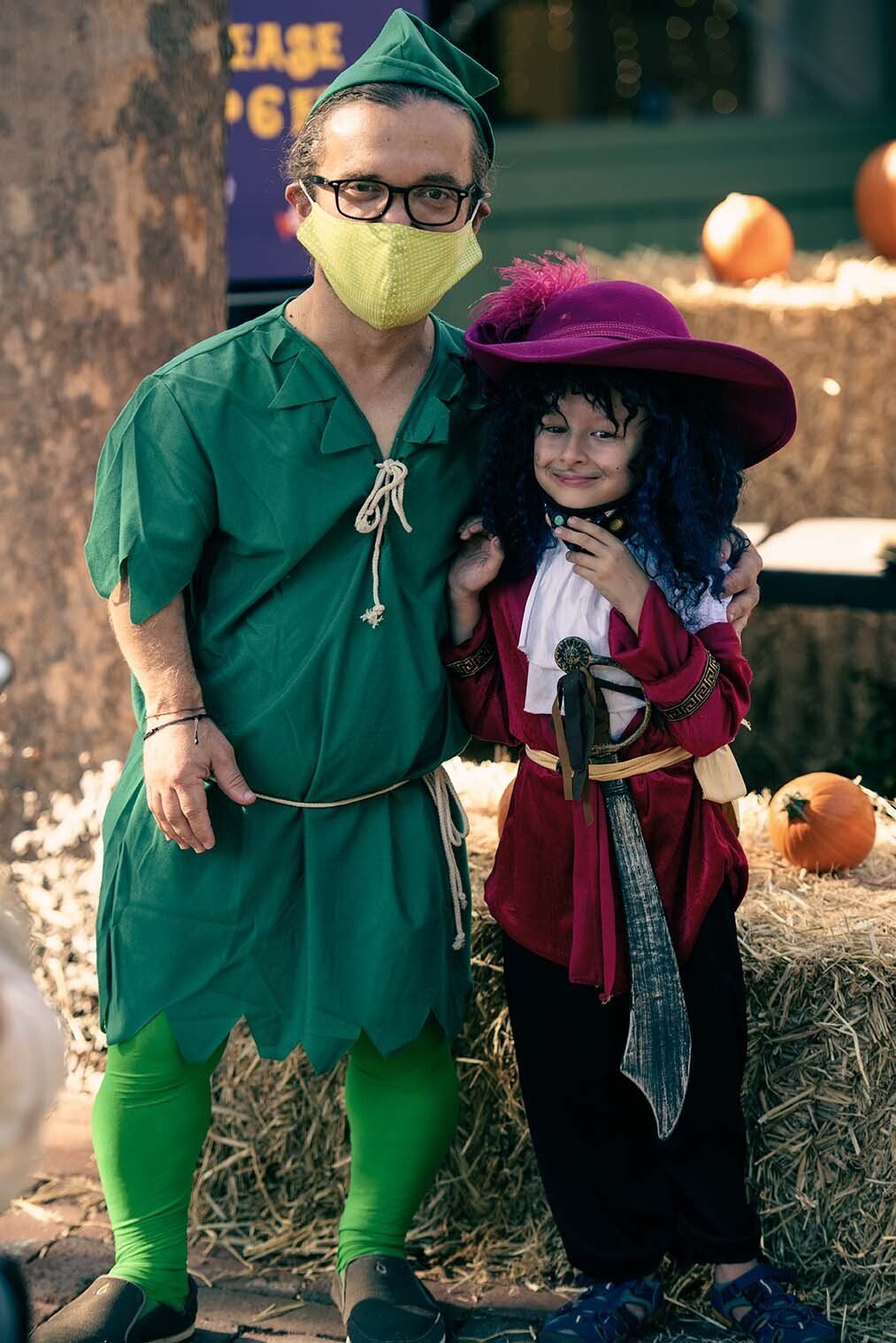 A man wearing a mask is standing next to a little girl in a peter pan costume