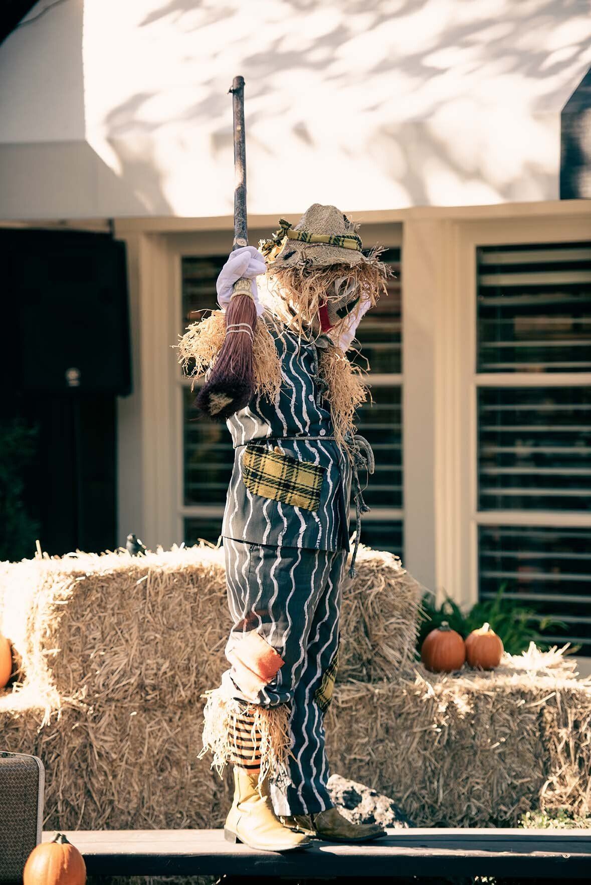 A scarecrow is standing in front of hay bales and pumpkins